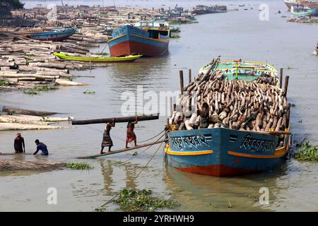 Swarupkathi, Pirojpur, Bangladesch. Dezember 2024. Auf dem größten schwimmenden Holzmarkt Bangladeschs in Swarupkathi im Bezirk Pirojpur tragen die Arbeiter große Holzstämme auf den Schultern. Das Gewicht jedes Stammes liegt zwischen 50 kg und 400 kg. Etwa 10.000 Arbeiter arbeiten auf diesem Holzmarkt und können 0 bis 5 pro Tag für diese harte Arbeit verdienen. Der Markt bietet eine große Auswahl an einheimischen Hölzern, darunter Mahagoni, Champagner und raintree. Händler aus dem ganzen Land kaufen auf diesem Upazila-Markt Holz im Wert von eineinhalb bis zwei Mrd. BDT. Diese Hölzer werden dann über V durch das ganze Land transportiert Stockfoto