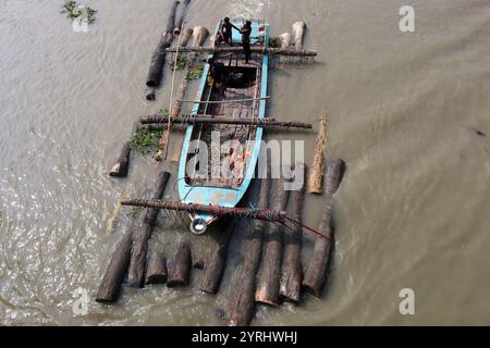 Swarupkathi, Pirojpur, Bangladesch. Dezember 2024. Händler kaufen Holz auf dem größten schwimmenden Holzmarkt in Bangladesch in Swarupkathi upazila im Bezirk Pirojpur und transportieren es in großen Booten. Der Markt bietet eine große Auswahl an einheimischen Hölzern, darunter Mahagoni, Champagner und raintree. Händler aus dem ganzen Land kaufen auf diesem Upazila-Markt Holz im Wert von einem Lakh-Dollar. Diese Hölzer werden dann auf verschiedenen Wegen durch das ganze Land transportiert, darunter LKW, Starts und Frachtschiffe. Tausende von Menschen in Swarupkathi sind tief in diese blühende Holzart verwickelt Stockfoto