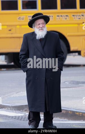 Ein chassidischer jüdischer Ältester wartet auf der Straße auf den nächsten Bus. An einem kalten Spätherbsttag in Williamsburg, Brooklyn, New York. Stockfoto