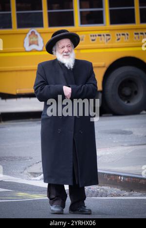 Ein chassidischer jüdischer Ältester wartet auf der Straße auf den nächsten Bus. An einem kalten Spätherbsttag in Williamsburg, Brooklyn, New York. Stockfoto