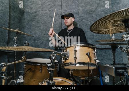Schlagzeuger in schwarzer Kappe, der auf hölzernem Schlagzeug in einem schalldichten Musikstudio auftritt. Stockfoto
