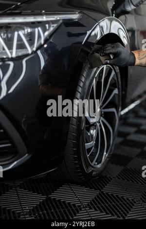Professioneller Mann, der Auto und Räder in der Garage wäscht. Detaillierung. Reifenpflege Stockfoto