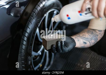 Professioneller Mann, der Reifenschwärzmittel auf den Pinsel im Detailservice aufträgt. Autowäsche und Radpflege Stockfoto