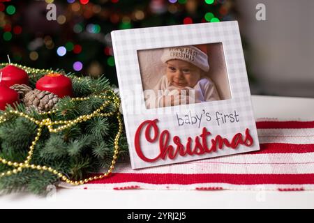 Ein Weihnachtsrahmen mit einem Babyfoto auf weißem Tisch und Adventskranz Stockfoto