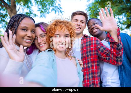 Verschiedene Freunde winken und lächeln im Freien in einem fröhlichen Selfie Stockfoto
