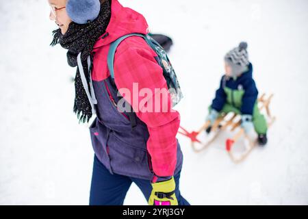 Mutter schleppt Schlitten mit dem Jungen im Schnee und Winter Stockfoto