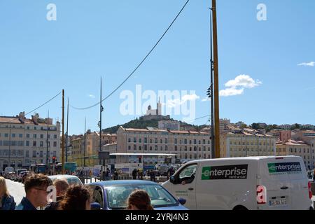 Marseille. Frankreich - 4. Dezember 2024: Eine geschäftige Straßenszene in Marseille mit der berühmten Basilika Notre-Dame de la Garde im Hintergrund, mit Stockfoto