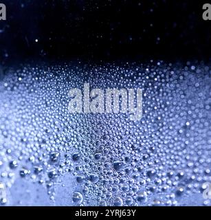 Blaue Regen-Blasen fallen auf einem feuchten Tag ein Fenster hinunter. Abstrakter Hintergrund Stockfoto