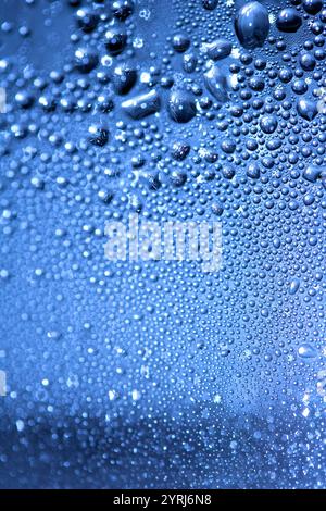 Blaue Regen-Blasen fallen auf einem feuchten Tag ein Fenster hinunter. Abstrakter Hintergrund Stockfoto