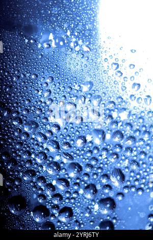Blaue Regen-Blasen fallen auf einem feuchten Tag ein Fenster hinunter. Abstrakter Hintergrund Stockfoto