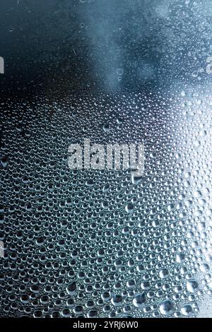 Blaue Regen-Blasen fallen auf einem feuchten Tag ein Fenster hinunter. Abstrakter Hintergrund Stockfoto
