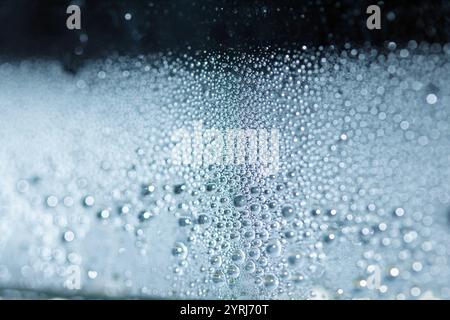 Blaue Regen-Blasen fallen auf einem feuchten Tag ein Fenster hinunter. Abstrakter Hintergrund Stockfoto