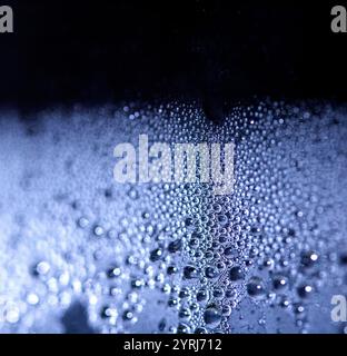 Blaue Regen-Blasen fallen auf einem feuchten Tag ein Fenster hinunter. Abstrakter Hintergrund Stockfoto
