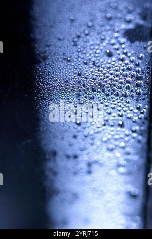 Blaue Regen-Blasen fallen auf einem feuchten Tag ein Fenster hinunter. Abstrakter Hintergrund Stockfoto