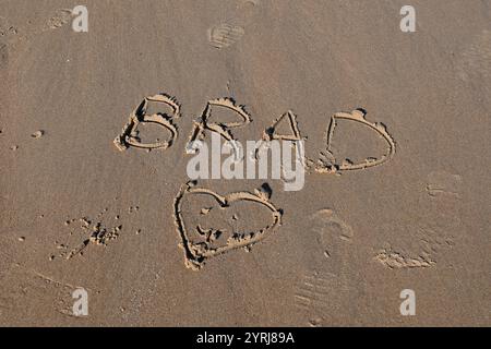 Der Name Brad wird in den Sand mit einem Herz darunter gezogen. Stockfoto