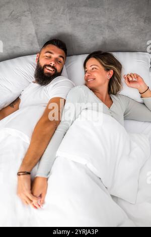 Das junge, glückliche Liebespaar liegt morgens im Bett. Sie sind entspannend und lächeln. Stockfoto