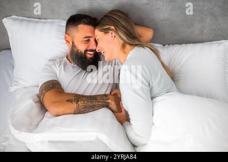 Das junge, glückliche Liebespaar liegt morgens im Bett. Sie sind entspannend und lächeln. Stockfoto