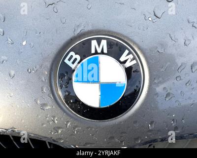 Nahaufnahme eines BMW-Logos auf einer Z3-Motorhaube mit Wassertropfen, das das ikonische blau-weiße reflektierende Licht zeigt Stockfoto