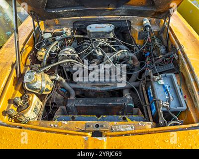 Reliant Scimitar GTE-Motortyp 1972 in einem gelben Fahrzeug mit offener Motorhaube, der detaillierte Komponenten und Verkabelung für die Autorestaurierung zeigt. Stockfoto