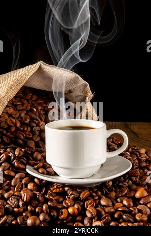 Tasse dampfenden Kaffee mit Beutel mit ungemahlenen Kaffeebohnen auf Holzoberfläche Stockfoto