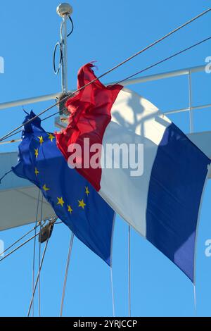 Die Flagge der Europäischen Union und der Franzosen winken auf einem Schiffsmast vor einem klaren blauen Himmel, wobei die Flagge der EU leicht abgenutzt erscheint und die Geschichte symbolisiert Stockfoto