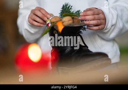 Stuttgart, Deutschland. Dezember 2024. Ein Mädchen greift nach einem Weihnachtsmann aus Schokolade in einem Stiefel voller Mandarinen, Nüssen und Zweigen. (Inszenierte Szene). Der Nikolaustag am 6. Dezember geht auf die Legende von zwei Bischöfen aus dem 4. Und 6. Jahrhundert zurück, deren gute Taten und Geschichten die Grundlage der Tradition bildeten. Quelle: Marijan Murat/dpa/Alamy Live News Stockfoto