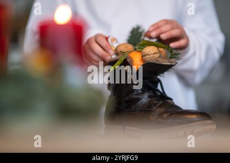 Stuttgart, Deutschland. Dezember 2024. Ein Mädchen greift nach einem Weihnachtsmann aus Schokolade in einem Stiefel voller Mandarinen, Nüssen und Zweigen. (Inszenierte Szene). Der Nikolaustag am 6. Dezember geht auf die Legende von zwei Bischöfen aus dem 4. Und 6. Jahrhundert zurück, deren gute Taten und Geschichten die Grundlage der Tradition bildeten. Quelle: Marijan Murat/dpa/Alamy Live News Stockfoto