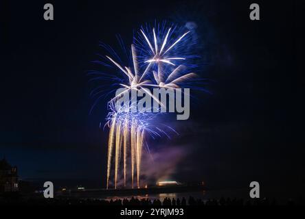 Silhouetten von Menschen, die das Feuerwerk über dem Meer beobachten. Blaues und weißes Feuerwerk. Neujahrsfeiern in Cromer, Norfolk, England, Großbritannien Stockfoto