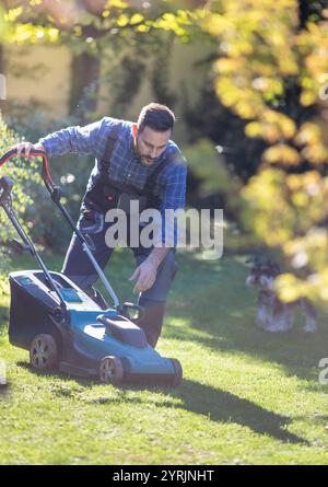 Hübscher Mann, der im Herbst den Rasenmäher mit Motor im Hinterhof anschaltet und sich um den Garten kümmert Stockfoto