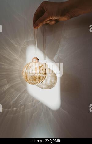 Frauenhand mit einem Vintage-goldenen Weihnachtsschmuck auf weißem Hintergrund mit Schatten. Minimalistische Komposition mit Fokus auf die Dekorati Stockfoto