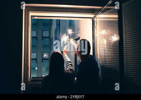 Silvester-Feuerwerk mit Fensterglitzern. Ein Paar, das zu Hause feiert. Eva Party mit Familie. Glitzern Sie in der Nacht. Glückliche Menschen zu Weihnachten. Silhouette von Stockfoto