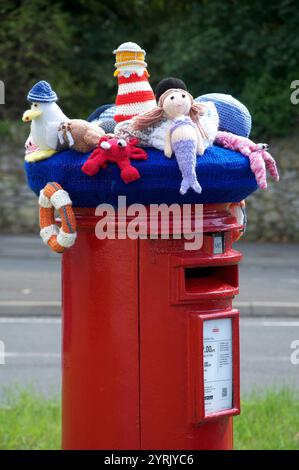 Ein farbenfroher Strickmütze aus Wolle mit Meeresmotiv und gehäkelten Möwen, Meerjungfrauen und anderen Meeresbewohnern ziert eine traditionelle rote Säulenkasten. UK. Stockfoto