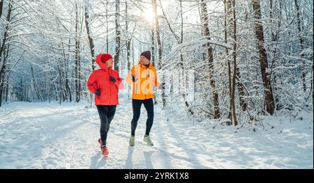 Lächelnde Läuferinnen und Läufer mittleren Alters trugen helle winddichte Jacken und liefen während der sonnigen Eiszeit im malerischen, schneebedeckten Wald Stockfoto