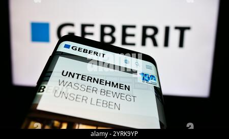 In dieser Fotoabbildung hält eine Person ein Smartphone mit dem Logo des Schweizer Sanitärunternehmens Geberit AG vor der Website. Stockfoto