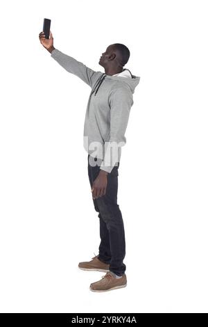 Seitliche Rückansicht eines Mannes, der ein Selbstporträt mit erhobenem Arm mit einem Smartphone auf weißem Hintergrund macht. Stockfoto