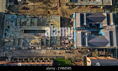 Luftaufnahme einer Baustelle mit zwei im Bau befindlichen Gebäuden, umgeben von Grundstücken und teilweise fertiggestellten Bauwerken. Erdarbeiten, Stockfoto