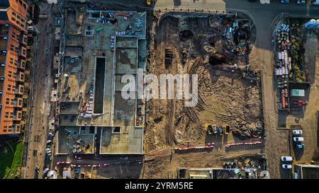 Luftaufnahme einer Baustelle mit Ausgrabungsfläche, teilweise fertiggestelltem Gebäude, Materiallager und angrenzenden Wohngebäuden. Th Stockfoto