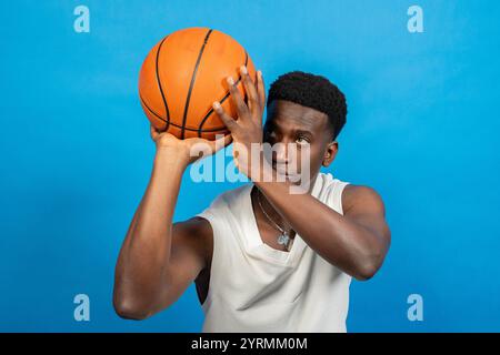 Junger Mann, der Basketball hält, konzentriert sich vor dem Schießen, vor leuchtendem blauem Hintergrund Stockfoto