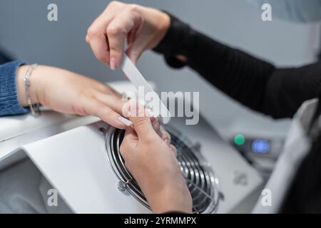 Frau professionelle Manikürerin, die Maniküre macht und Nagelfeile mit Nagelfeile im Schönheitsstudio feilt, Nahaufnahme. Hand- und Nagelpflege Stockfoto