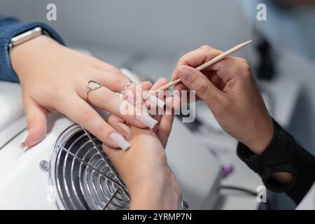 Professionelle Manikürerin, die im Schönheitssalon Maniküre und Nagelhaut mit Holzstab schneidet. Hand- und Nagelpflege Stockfoto