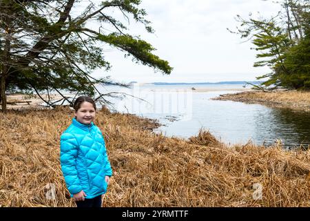 Mädchen posiert für die Kamera mit Hamline Lake dahinter während einer Wanderung im Ludington State Park im Frühjahr in der Nähe von Ludington, Michigan, USA. Ludington Street Stockfoto