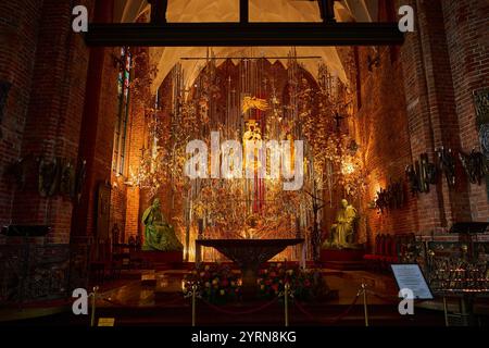 Ein kunstvoll verziertes Innere einer Danziger Kirche mit einem atemberaubenden Altar, der mit goldenen Bernsteinskulpturen, Blumendekorationen und Statuen geschmückt ist, beleuchtet von Stockfoto