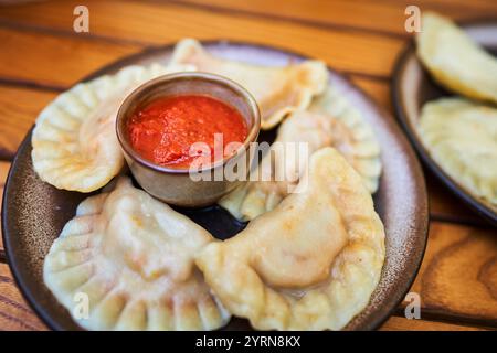 Ein Teller mit traditionellen polnischen Knödeln, serviert mit einer Seite mit gewürfeltem Speck, auf einem Holztisch. Stockfoto