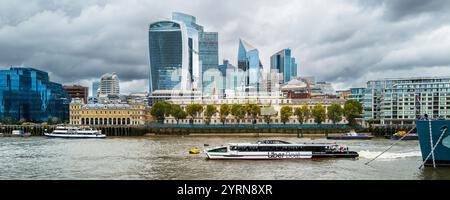 Ein Panoramabild eines Thames Clipper Uber Bootes, das flussaufwärts auf der Themse an berühmten Gebäuden der City of London im bac vorbeifährt Stockfoto