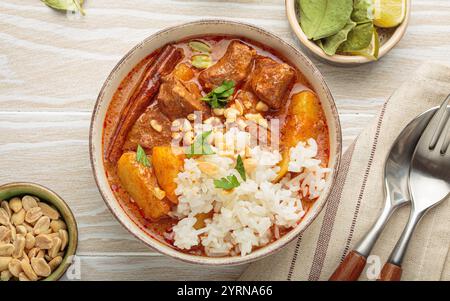 Köstliches Massaman-Curry mit Rindfleisch, Kartoffeln, Reis und Erdnüssen auf weißem Holzhintergrund, traditionelle thailändische Küche Stockfoto