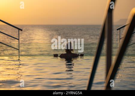 Silhouette einer Frau, die sich am Rand des Infinity-Pools auf dem Achterdeck des Expeditionskreuzfahrtschiffs SH Diana (Swan Hellenic) bei Sonnenuntergang bei s entspannt Stockfoto