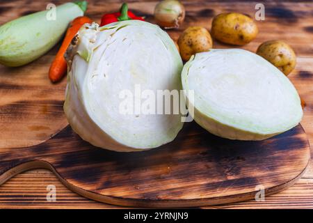 Weißkohl, in zwei Hälften oder Stücke geschnitten, auf einem Holztisch mit Kartoffeln, Paprika, Karotten und Zucchini. Hochwertige Fotos Stockfoto