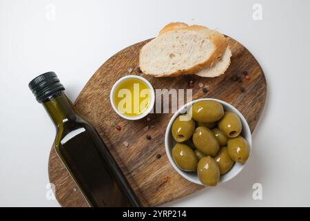 Bio-Olivenöl in der Schüssel mit grünen Oliven und Ciabatta-Brot auf weißem Hintergrund, Blick von oben, Kopierraum. Gesundes mediterranes Lebensmittelkonzept. Stockfoto