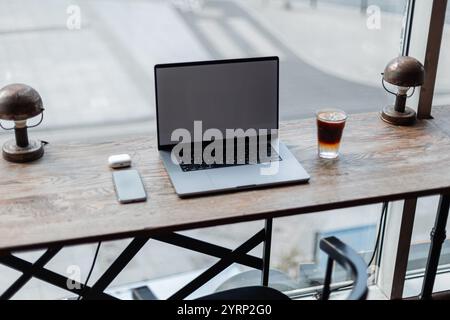 Laptop mit Smartphone, Kopfhörern und Kaffee Espresso Tonic steht auf Holztisch im Café. Freiberufliche und externe Arbeit. Kreative Idee. Notebook-Modelle Stockfoto