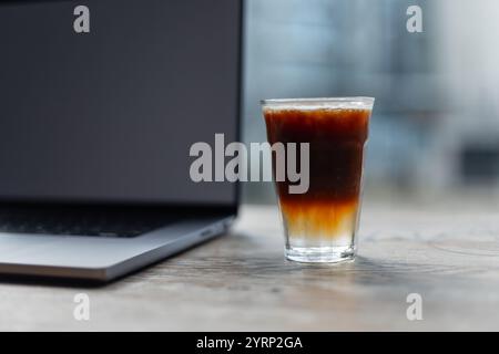 Duftender köstlicher frischer Espresso Tonic Kaffee steht auf einem Holztisch mit Laptop. Guten Morgen und den Beginn der Arbeit. Zeit für Energie. Stockfoto